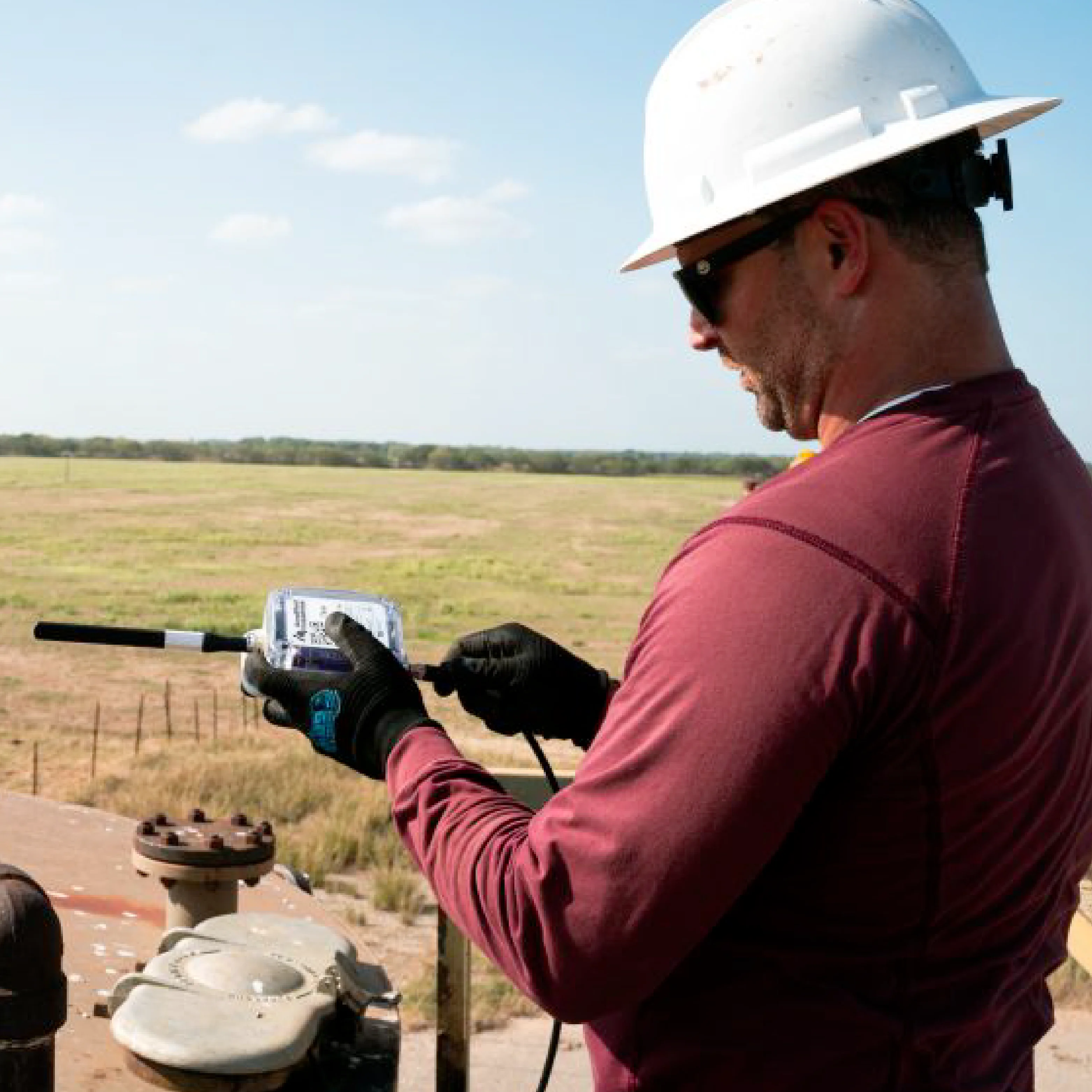 Pumper in gloves holding an Amplified wireless device at a wellhead